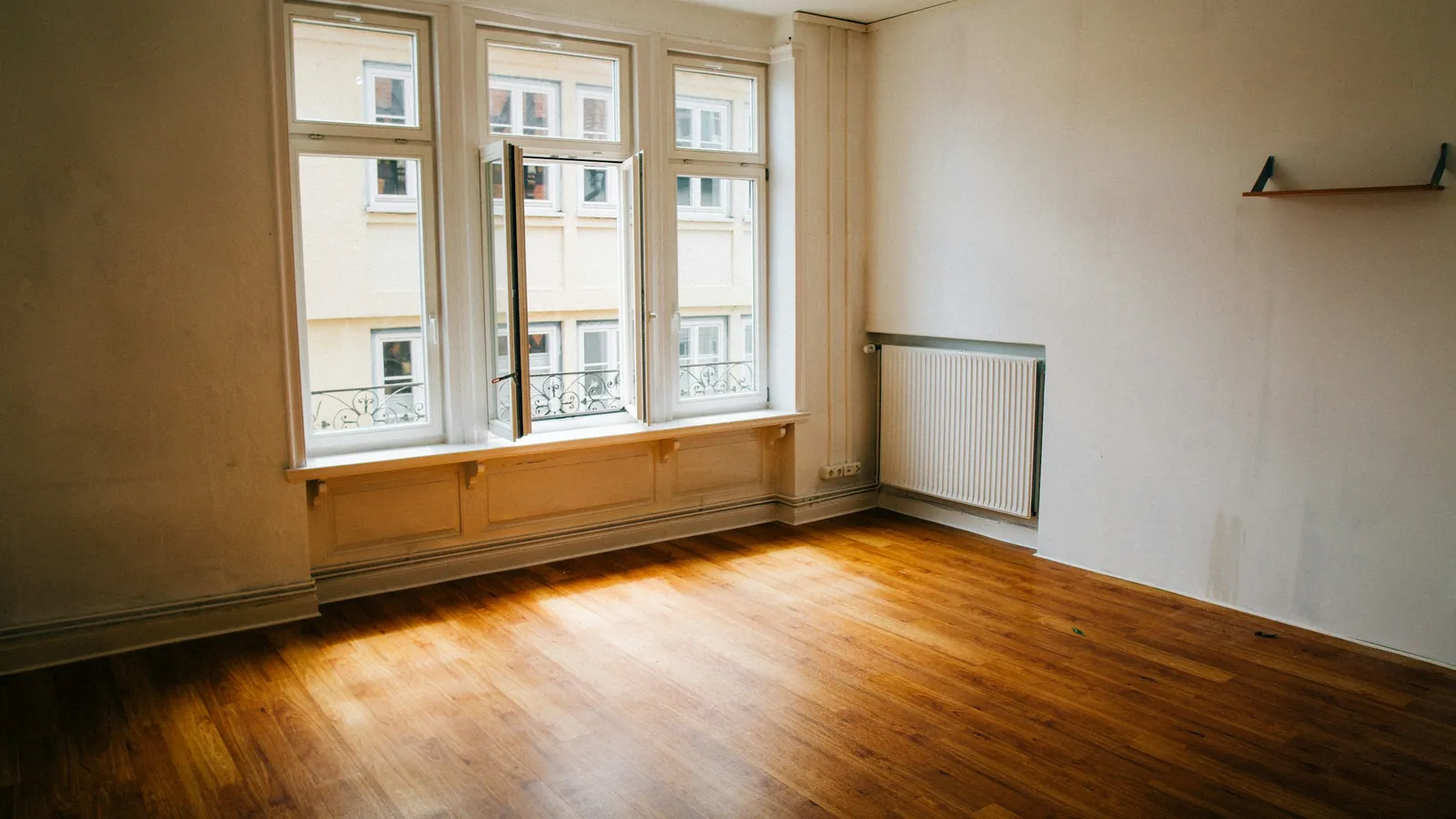 Pièce vide et lumineuse, parquet et grandes fenêtres, dans un immeuble ancien