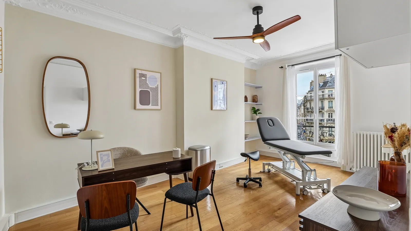 Cabinet de consultation lumineux dans un immeuble haussmannien, table d'examen, bureau en bois sombre, chaises et vue sur les façades parisiennes